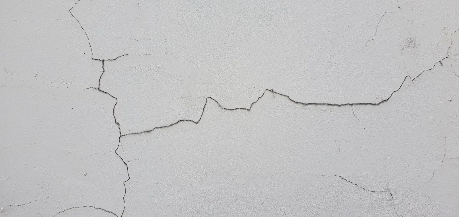 Long horizontal fissure across a white painted cement wall