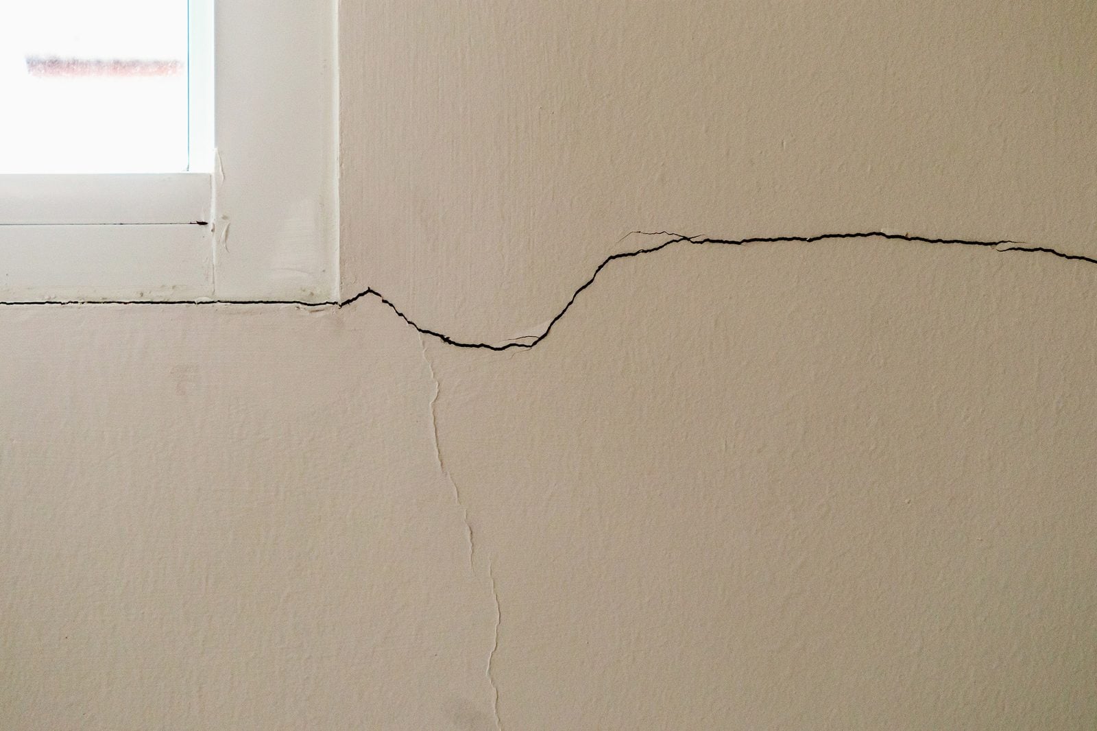 Long settlement crack running across a wall below a window